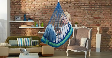 Young woman using laptop, sitting in hammock like chair in retro home.